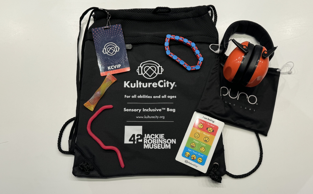 A black drawstring bag with a set of headphones, fidget tools, and lanyard cards displayed on top of it.
