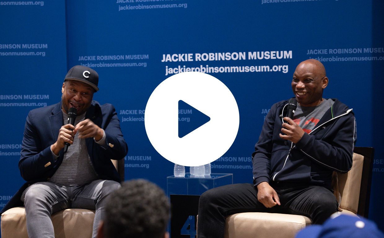 A photo of two panelists seated on stage in front of a blue Museum backdrop. 